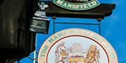 A pub sign showing the crest for "The Manchester Arms" and the name "The Mansfield Brewery Company" below, with a colorful coat of arms featuring a un