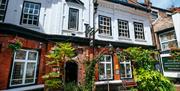The exterior of Ye Olde White Harte, a beautiful red and white brick building with several windows, an open doorway and multiple plants decorating a s