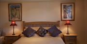 A cosy bedroom with a wooden headboard bed, three decorative pillows, cream bedding, two bedside tables with matching red lamps, and framed art hangin