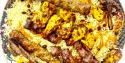 A large decorative platter filled with yellow rice topped with various grilled meats, including kebabs, chicken, and lamb chops, as well as roasted to
