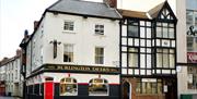 A street view of the Burlington Tavern, a traditional British pub and hotel with a black and white exterior, arched windows, and a bright red door on