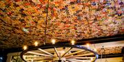 Interior of The Lion and Key, with a ceiling completely covered in colorful beer mats and coasters, featuring a large wagon wheel chandelier and a rou