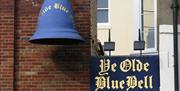 An exterior shot of the alley leading to Ye Olde Blue Bell. On the corner of a brick wall is a blue sign and a blue bell both featuring gold writing t