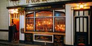 Nighttime street view of "Ye Olde Black Boy" pub with illuminated signage, hanging plants, and vintage-style windows and doors.