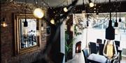 Cozy restaurant interior of Sleepers Bar with exposed brick walls, hanging Edison bulbs, string lights, dark wooden tables, and black chairs. A large
