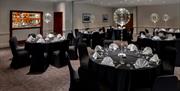 Function room with tables dressed in black with white napkins and balloons on the table.