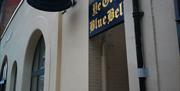 An exterior shot of the alley leading to Ye Olde Blue Bell. On the corner of a cream coloured brick wall is a blue sign and a blue bell both featuring