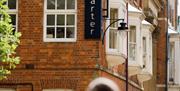 A person walks down a street with victorian architecture with a large sign on the corner of the building reading 'The Museum Quarter'