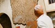 A man looks at a section of mosaic suspended on a wall.