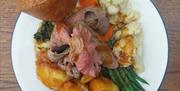 A plate of traditional roast dinner featuring slices of roast beef with gravy, roast potatoes, green beans, carrots, cauliflower cheese, and a Yorkshi