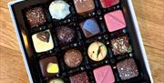 A selection of sixteen chocolates in a white, square box on a wooden table.