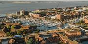 Aerial view of Hull marina filled with sailing boats and yachts, surrounded by red-brick buildings and roads, with a river and industrial waterfront s