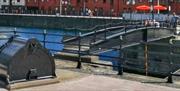 View of Hull Marina showing black metal pontoon walkways and moorings on calm blue water, with waterside red-brick buildings, railings, and bright red