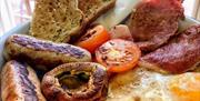 A plate filled with staples of a full english breakfast, such as hash browns, eggs, bacon, tomatoes, sausages, wholemeal toast and mushrooms.